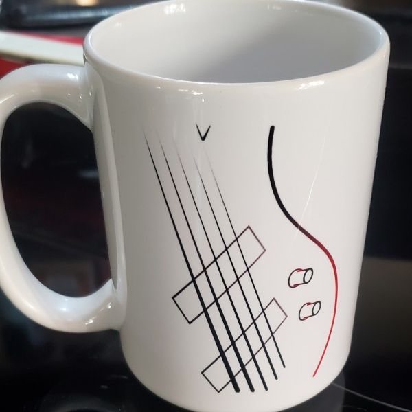 A big coffee mug with line art of a 5-string Ibanez bass guitar